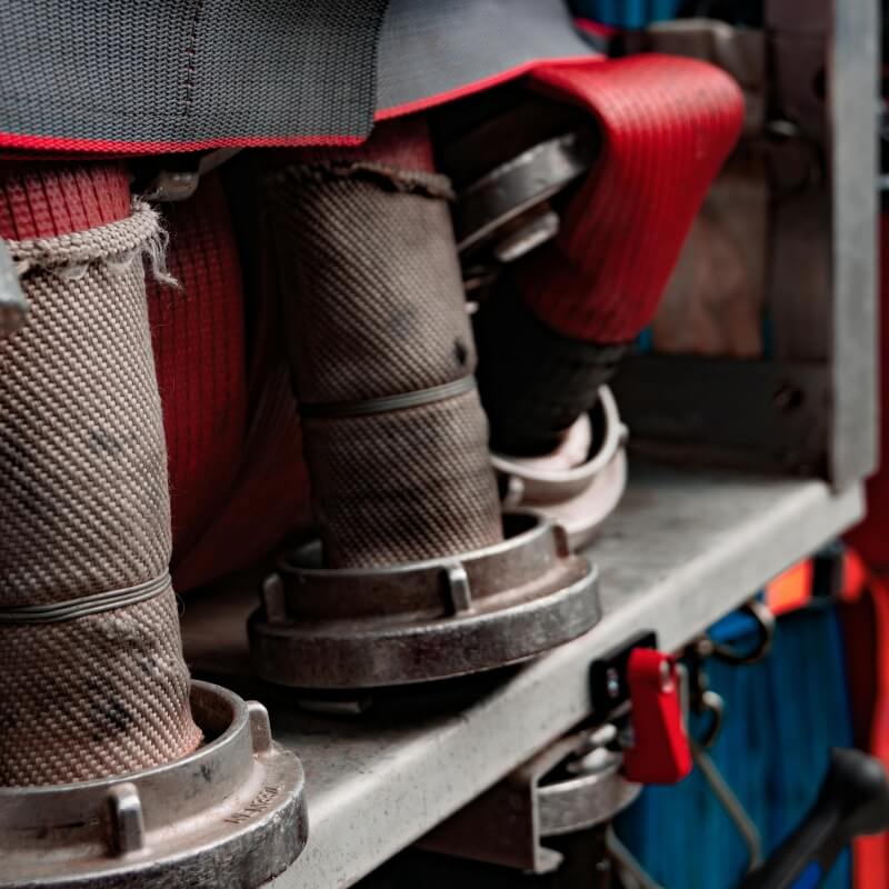 Close-up of fire hoses and couplings secured on a vehicle, with red straps and metal clamps visible.