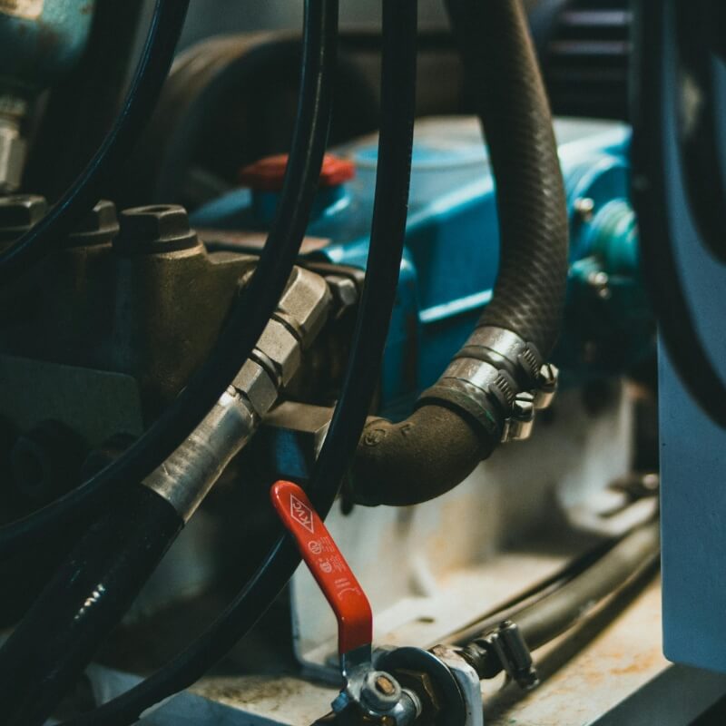 Close-up of hydraulic hoses and metal fittings on industrial machinery, with a red valve lever in the foreground.