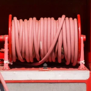 Pink fire hoses neatly coiled around a red hose reel on a fire truck or equipment rack, ready for use.