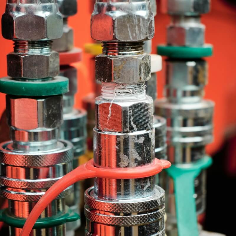 Close-up of metal hydraulic quick-connect fittings with colored seals (green and red) in a workshop.
